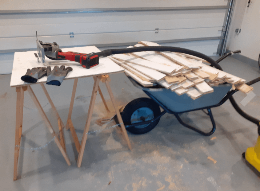 Mini scie circulaire Einhell TC-TS 860 Test | Avis 2 photo de la mini scie circulaire Einhell TC TS 860 posée sur une table en bois avec des gants de sécurité, branché à un aspirateur à poussière avec une brouette pleine de morceau de bois à côté