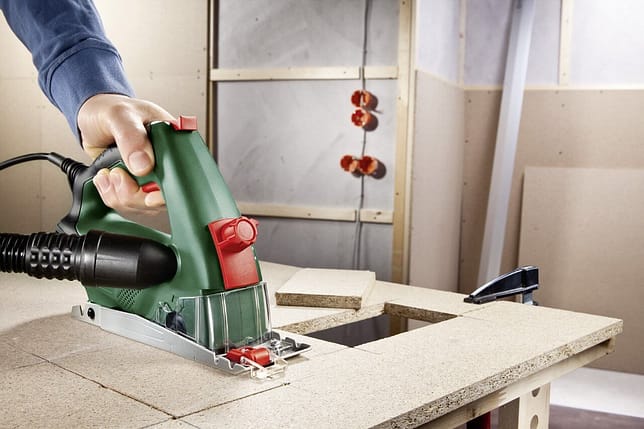 Mini scie circulaire Bosch Universal PKS 16 Test | Avis 2 Photo de la mini scie circulaire manuelle bosch universal PKS 16 tenu par quelqu'un en train de couper une planche de bois